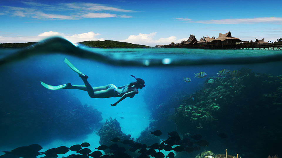 a beautiful lady in a bikini submerged in a blue ocean perfectly calm and looking at fish near the cave